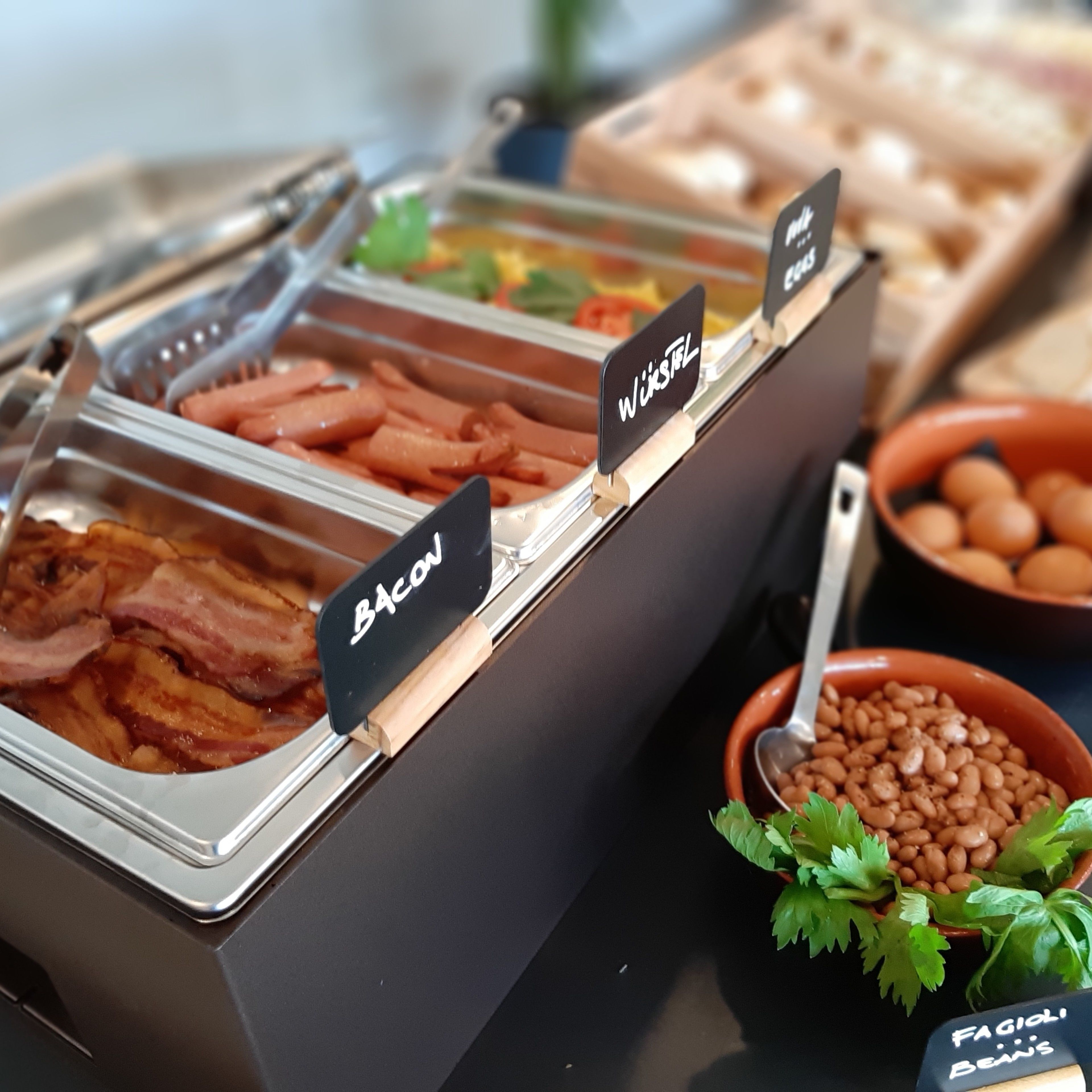 A buffet with labeled sections for bacon, waffles, and beans.
