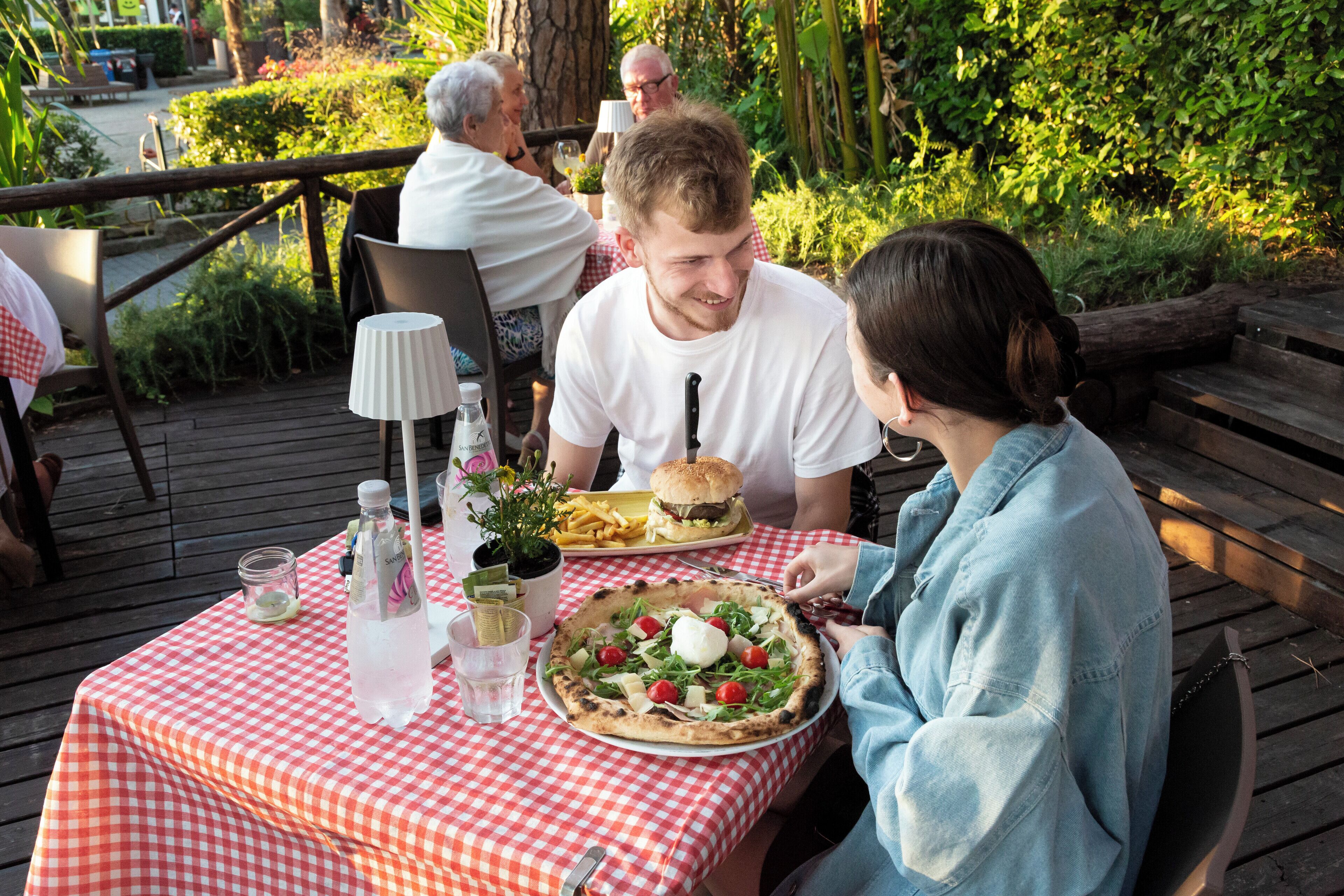 Un tavolo da pranzo con una tovaglia a quadretti, una pizza, un hamburger e una bevanda.