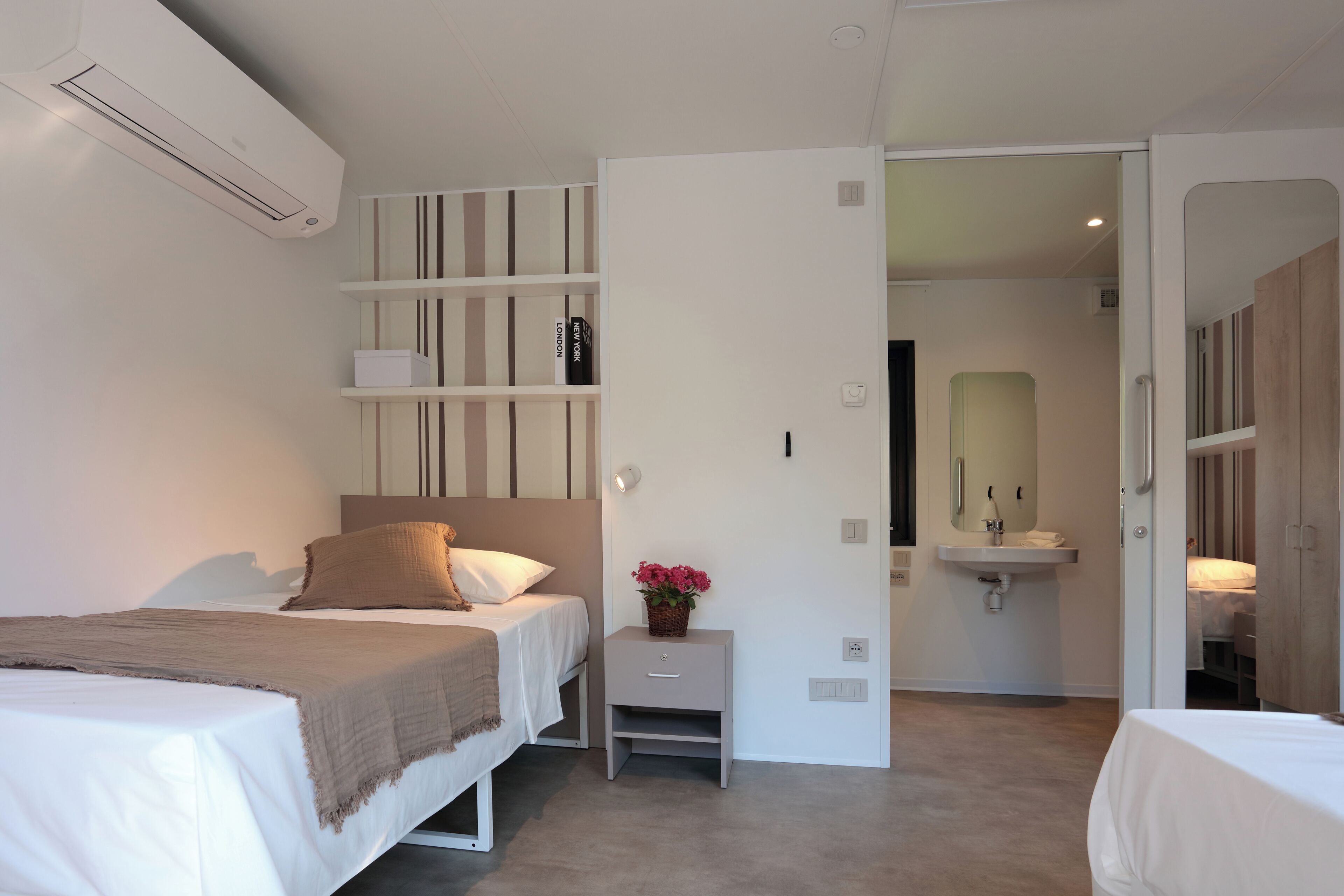 A modern hotel room with a bed, bedside table, and a small wall-mounted shelf.