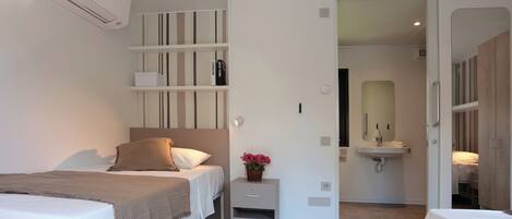 A modern hotel room with a bed, bedside table, and a small wall-mounted shelf.