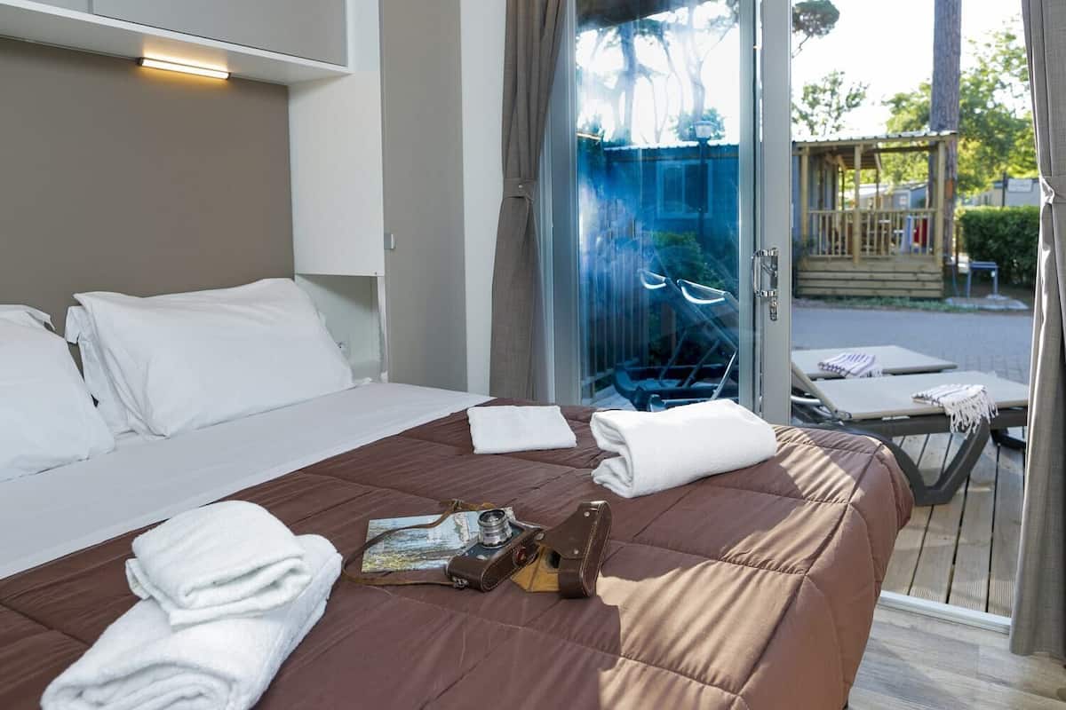 A hotel room with a bed, a table with a chair, and a view of the outside.