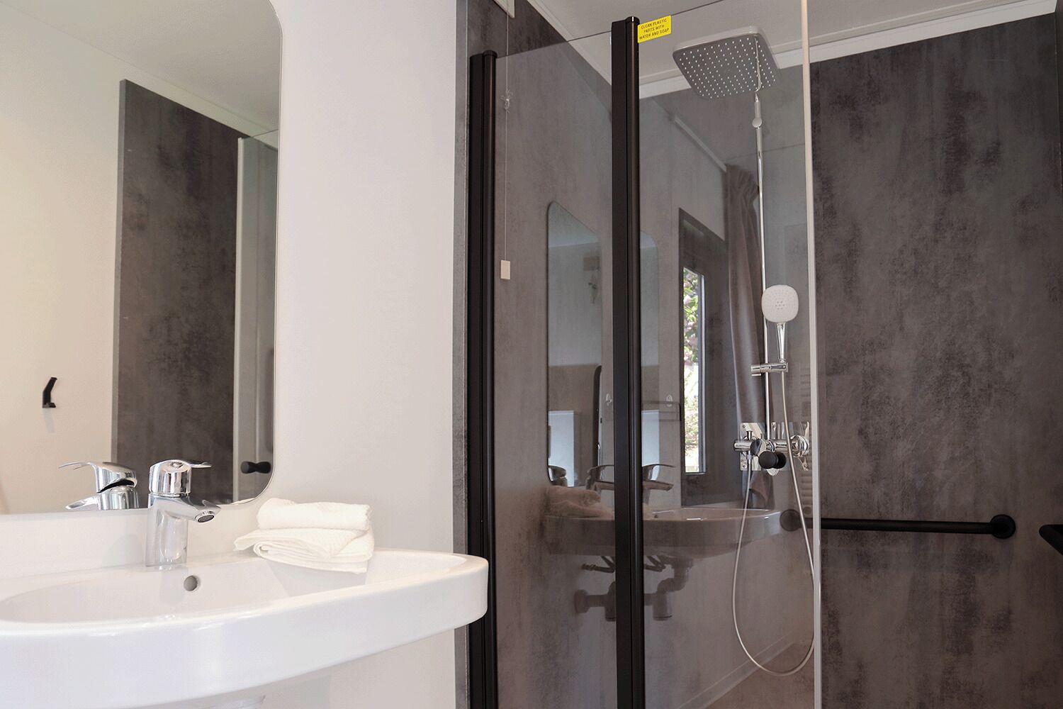 A modern bathroom with a glass-enclosed shower, a white sink, and a large mirror.
