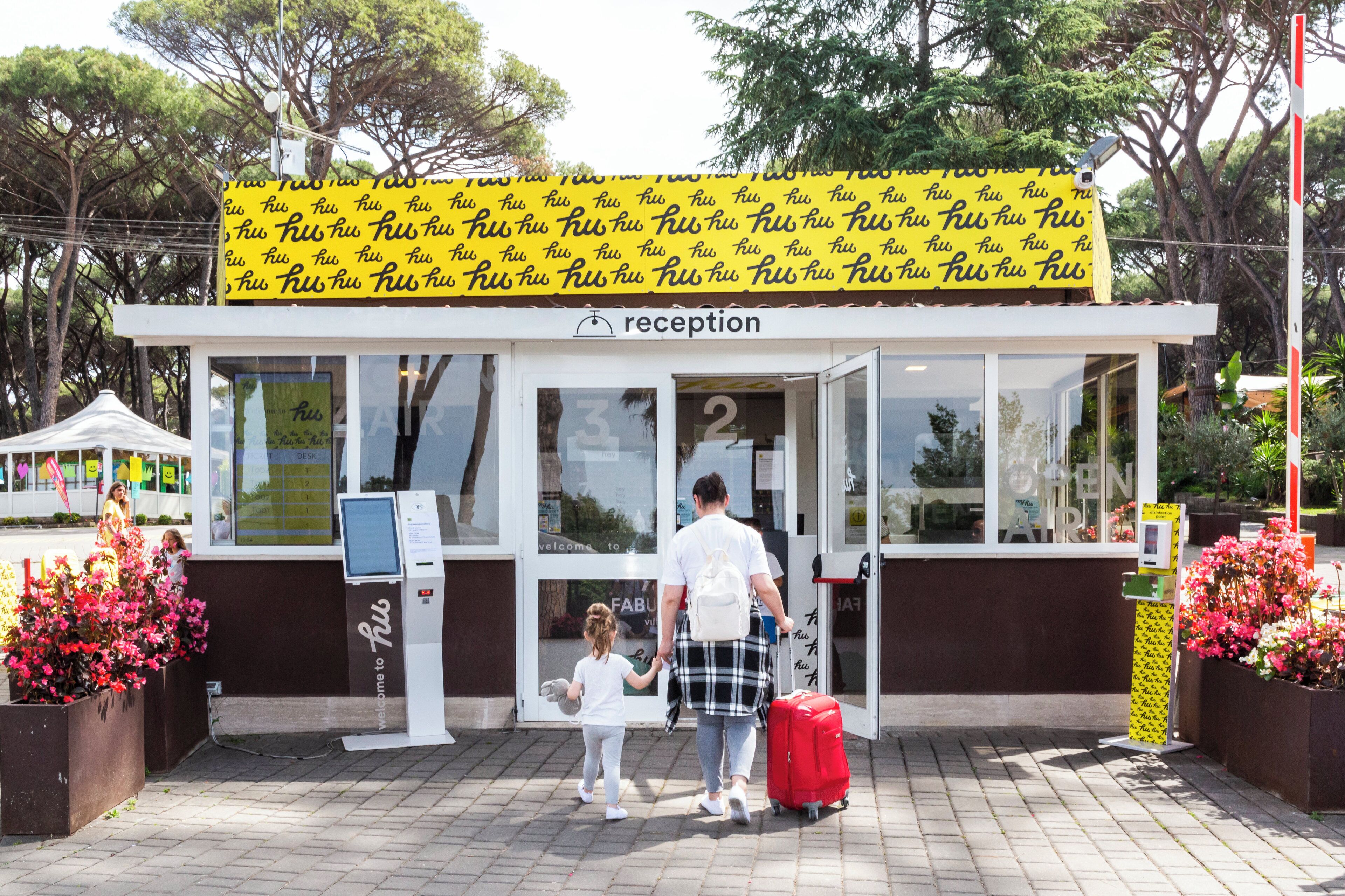 Een receptie met een grote gele banner, een ticketautomaat en een bagagewagen.