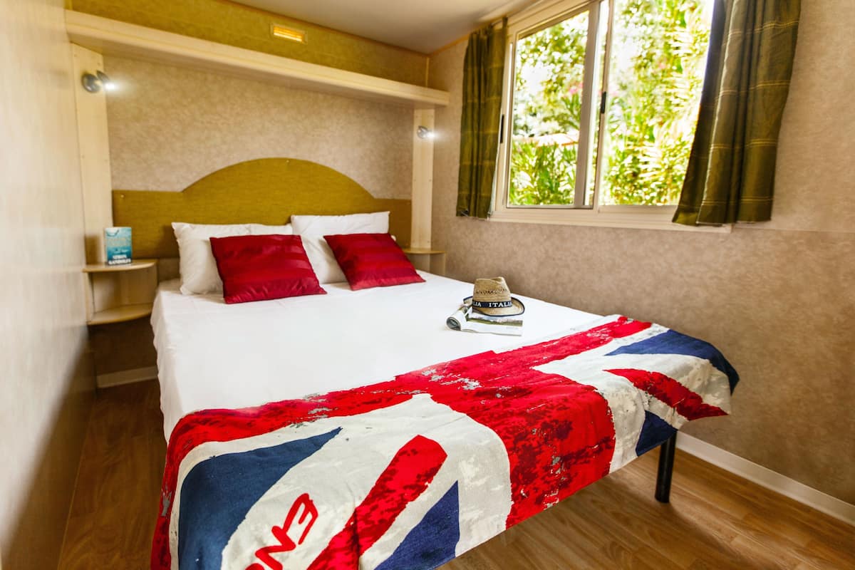 A neatly made bed with a red, white, and blue blanket, a wooden headboard, and a window with curtains.