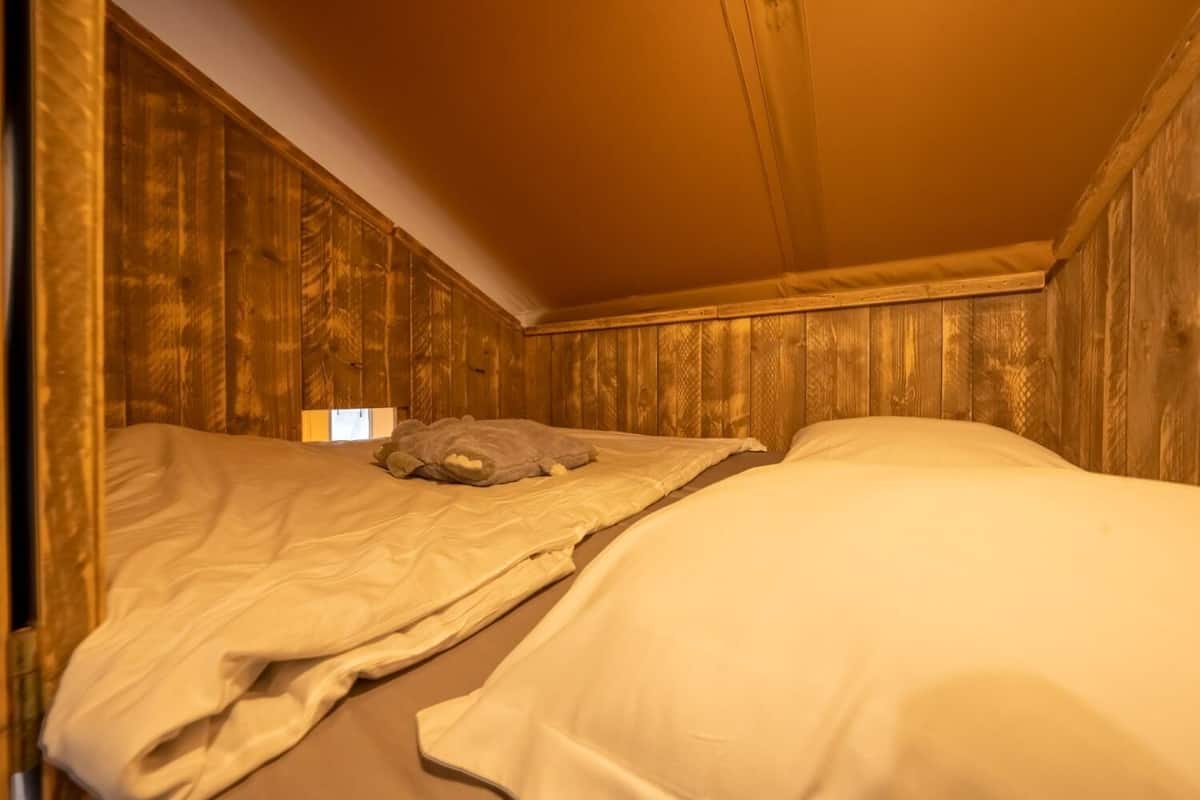 A small, cozy room with wooden walls and a sloped ceiling. There are two beds with white bedding and a gray pillow on one bed.