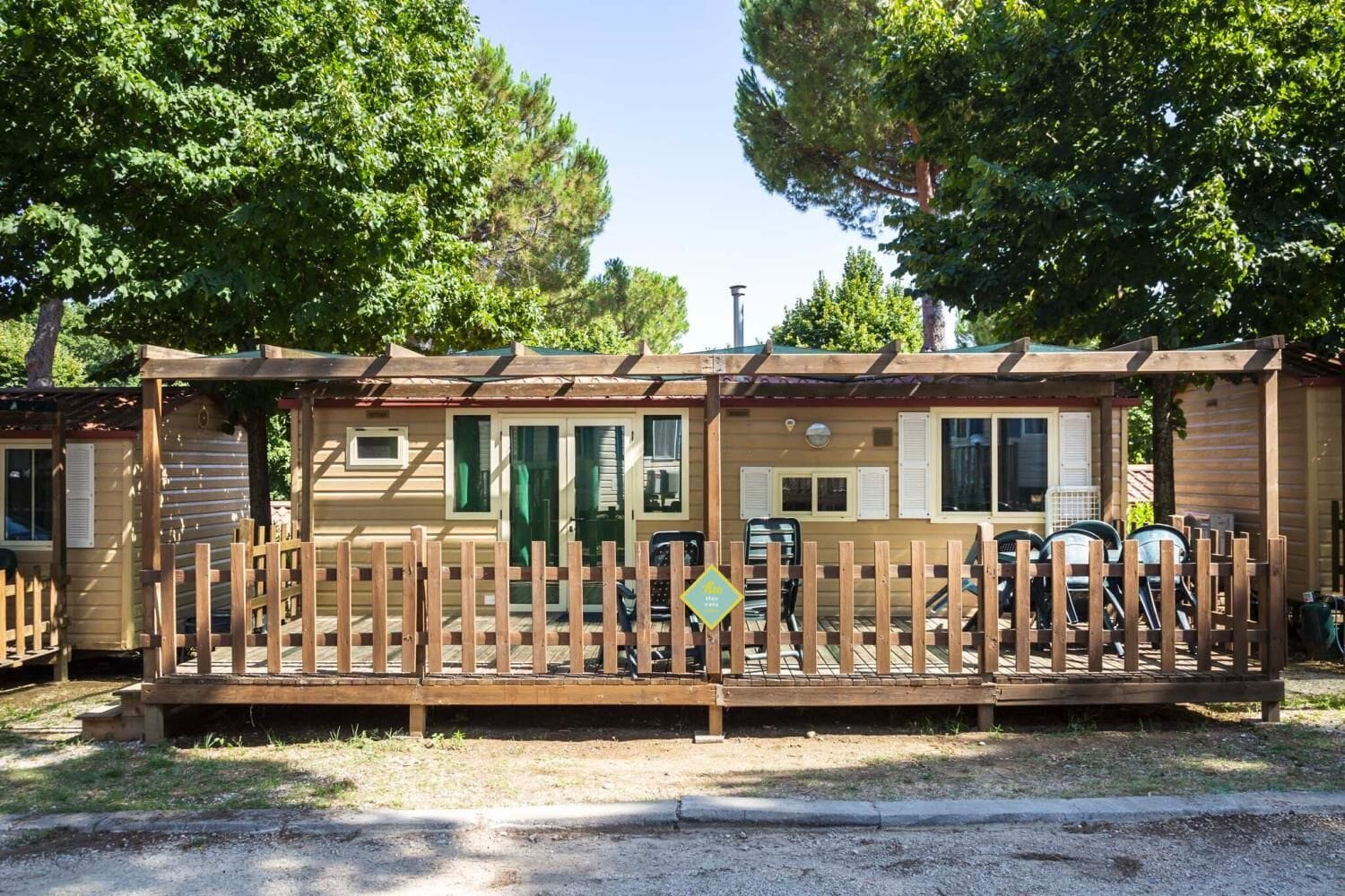 Een houten chalet met een omheind terras, een overdekte veranda en een klein bijgebouw.