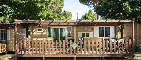 Een houten chalet met een omheind terras, een overdekte veranda en een klein bijgebouw.