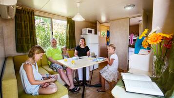 Une famille de quatre personnes est assise autour d’une table dans un petit espace de vie comprenant un coin cuisine, un canapé et un coin repas.
