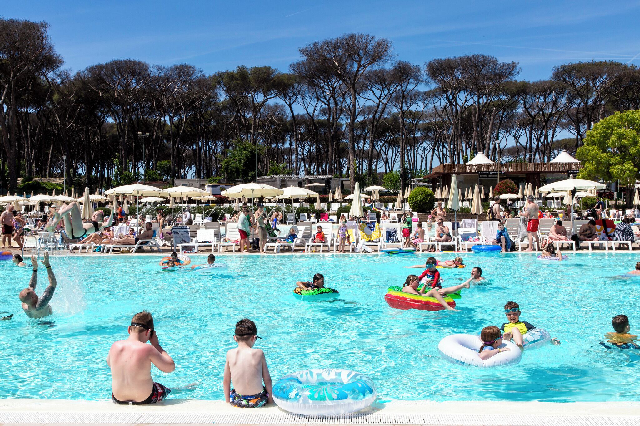Un espace piscine agrémenté de chaises longues et de parasols, entouré d’arbres.
