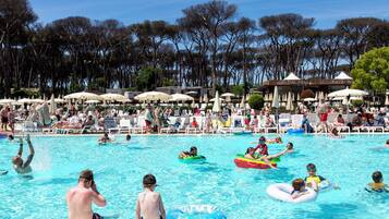 Un espace piscine agrémenté de chaises longues et de parasols, entouré d’arbres.