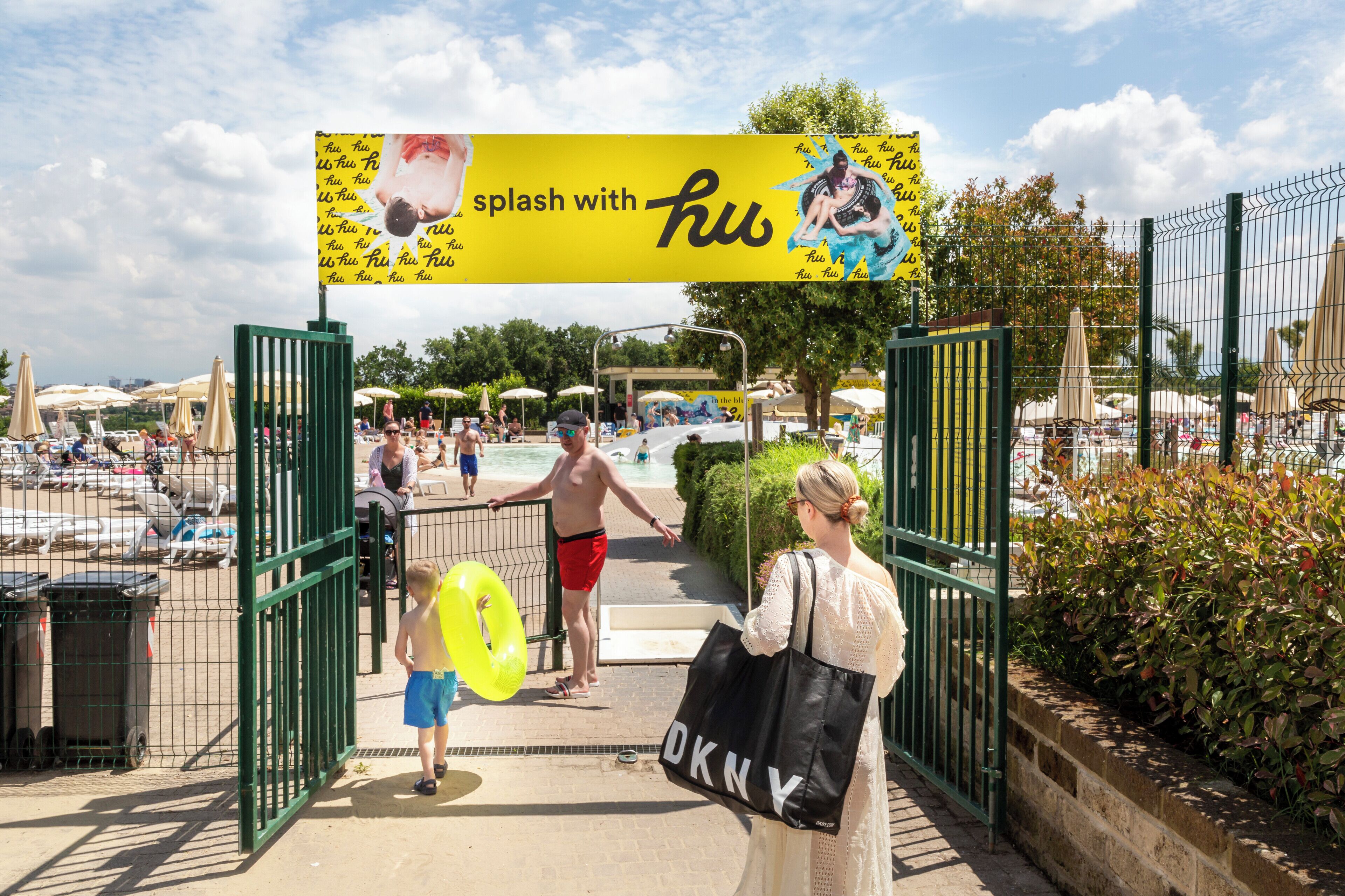 Ein Strandzugang mit einem 'Splash with H2O'-Schild, einem Poolbereich und Sonnenschirmen.
