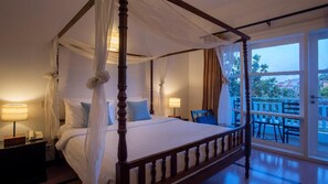 A four-poster bed with a canopy, a nightstand with a lamp, and a view of the outdoors through a glass door. - Amber Angkor Villa Hotel & Spa (Siem Reap)