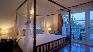 A four-poster bed with a canopy, bedside lamps, a view of the outdoors, and a balcony with chairs. - Amber Angkor Villa Hotel & Spa (Siem Reap)