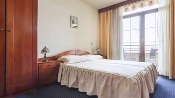 Een hotelkamer met een bed, een houten kledingkast, twee nachtkastjes met lampen, een raam met gordijnen en een klein schilderij aan de muur.