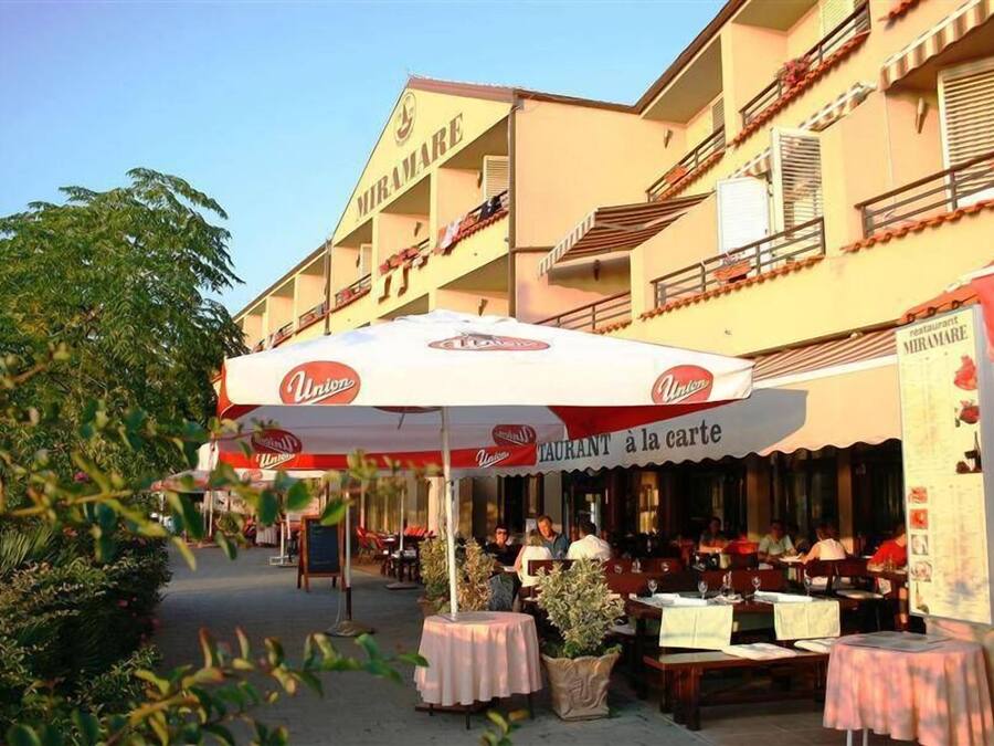 Un restaurante llamado 'Miramare' con mesas al aire libre y una sombrilla blanca.