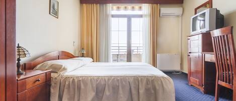 Een hotelkamer met een bed, een houten nachtkastje, een bureau met stoel, een televisie op een kast en een raam met gordijnen.