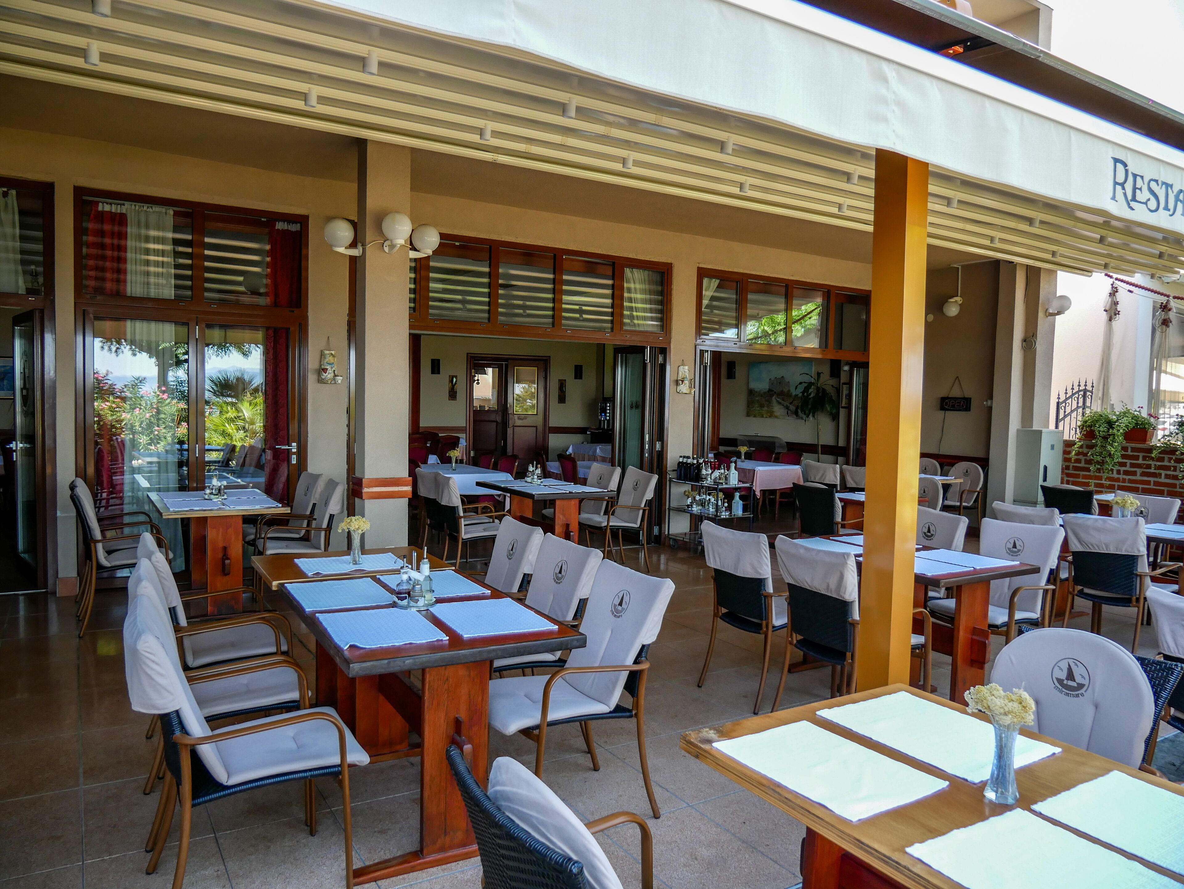 Un restaurante con terraza, mesas, sillas y un cartel que indica que está abierto.