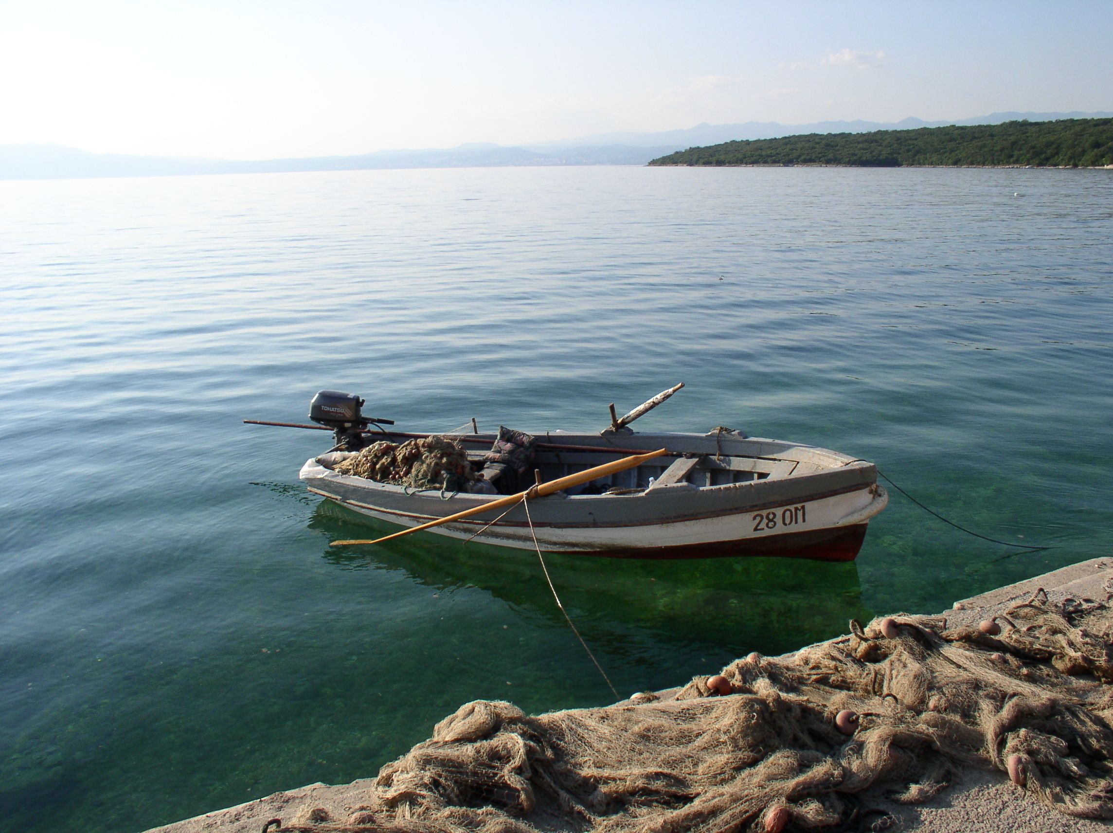 Ein kleines Boot mit der Aufschrift 28.0m liegt in ruhigem Wasser vor Anker.