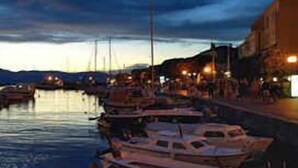 A marina with several boats docked, a waterfront promenade, and buildings along the shore.