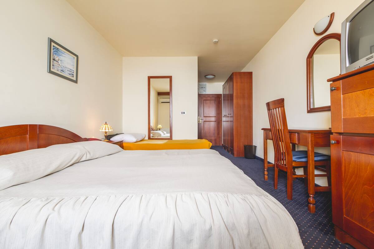Ein Hotelzimmer mit einem großen Bett, einem Holztisch, einem Stuhl, einer Kommode und einem Spiegel.