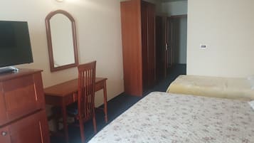 A hotel room with a bed, a desk with a chair, a wardrobe, and a mirror.