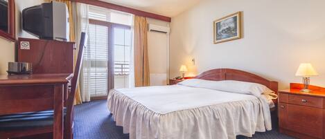 A hotel room with a bed, a desk, a chair, a TV, a lamp, and a painting on the wall.
