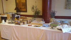 A buffet table with various food items and containers, including a fruit bowl, a green dish, and a clear container with food.