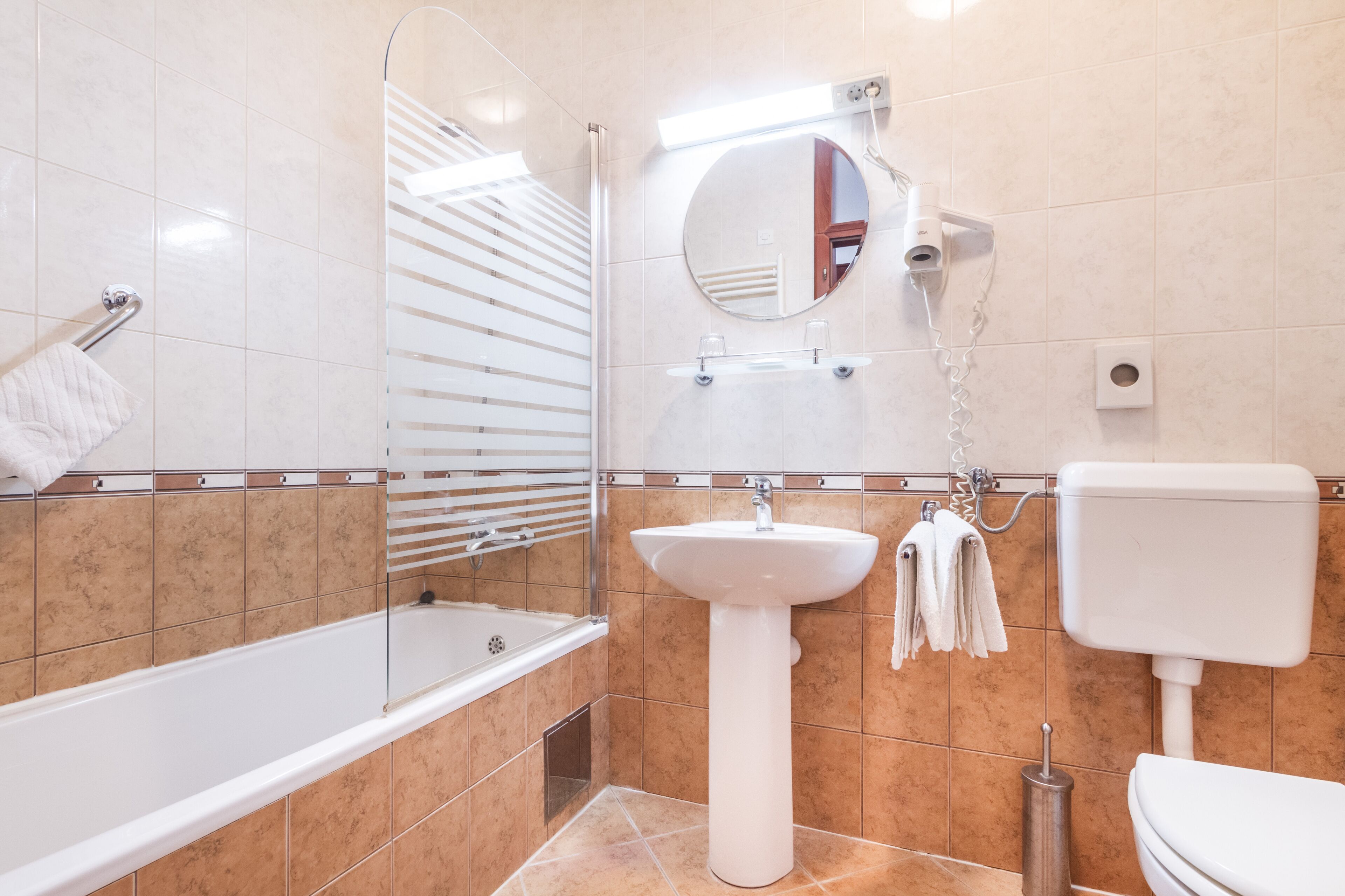 A modern bathroom with a bathtub, a pedestal sink, a toilet, and a shower with a glass door.