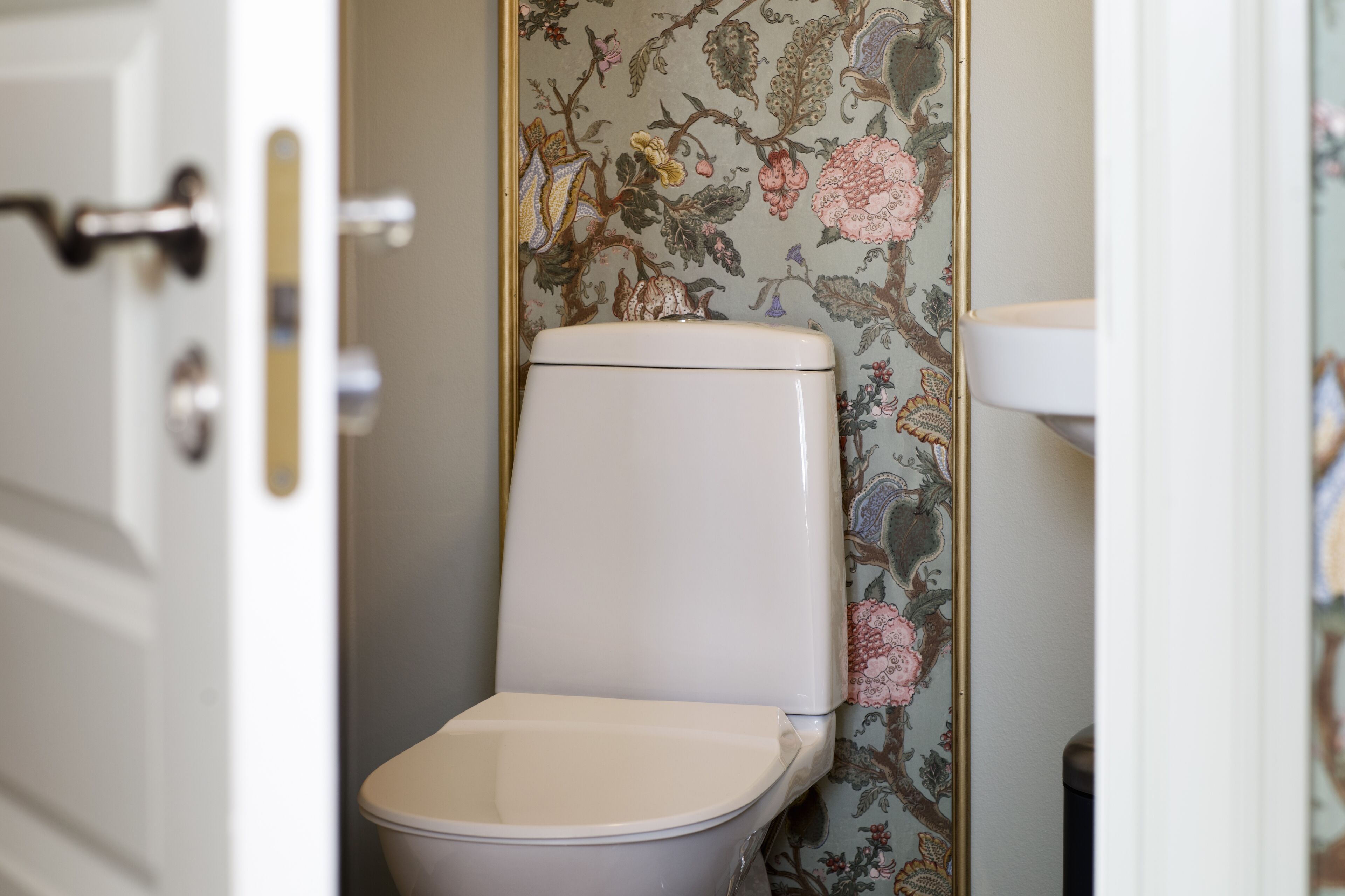 Casa de banho com sanita, lavatório e papel de parede floral.