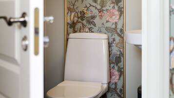 Casa de banho com sanita, lavatório e papel de parede floral.