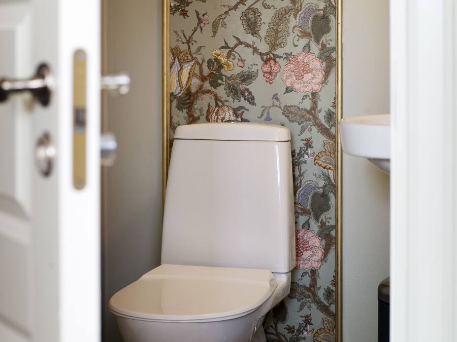 Casa de banho com sanita, lavatório e papel de parede floral.