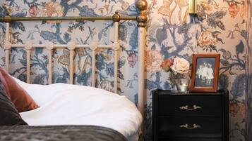 A neatly made bed with a white comforter and a brown pillow, a black nightstand with drawers, a framed picture, and a vase with flowers.