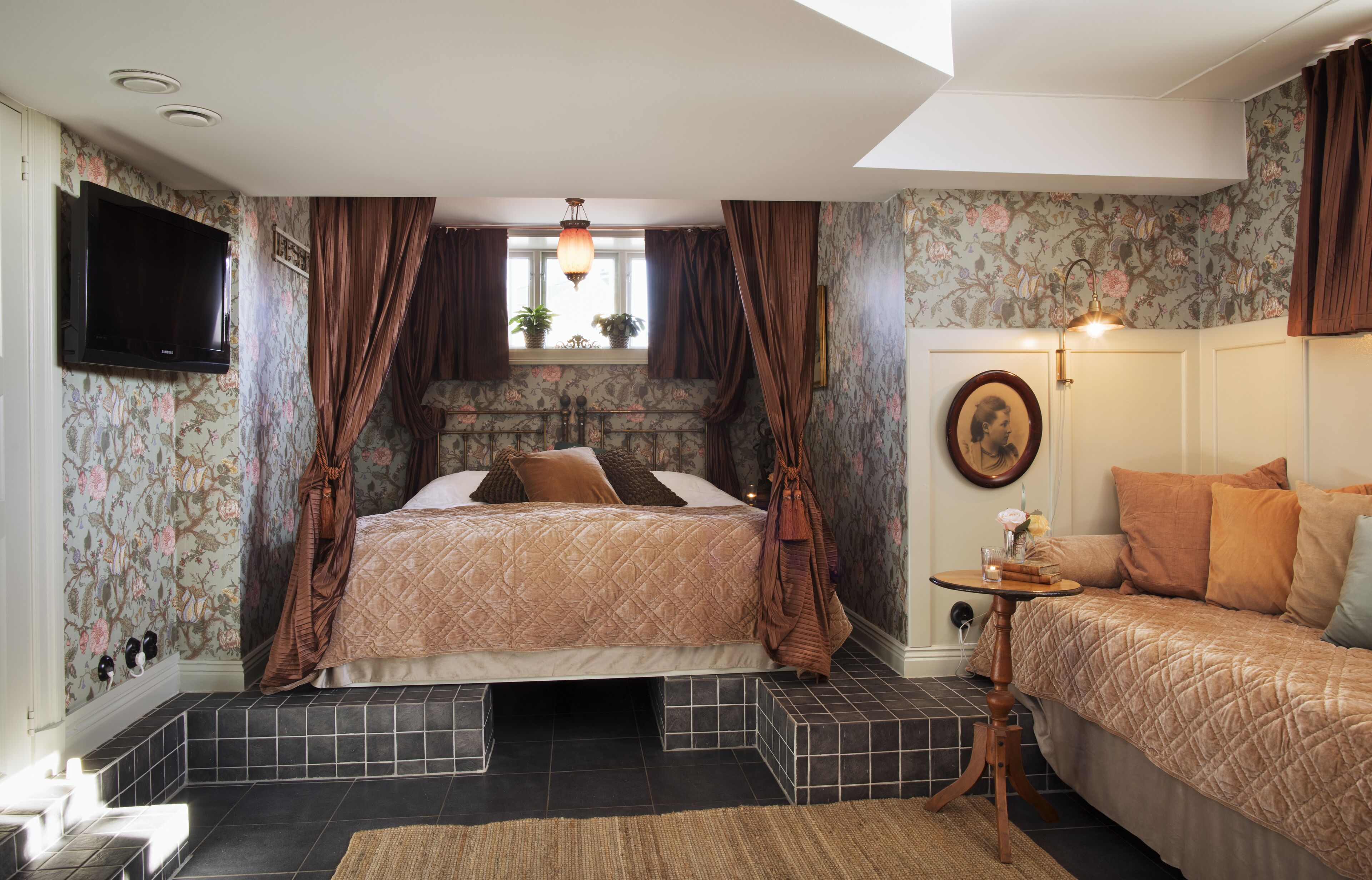 A bedroom with a bed, a sofa, a television, and a window with curtains.