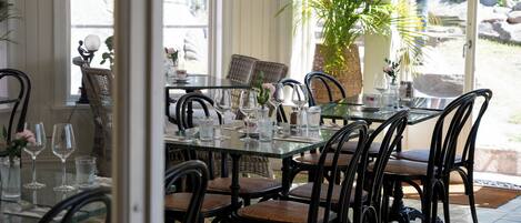 A dining area with glass tables and wicker chairs, a potted plant, and a view of the outdoors.