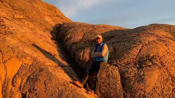 A person sitting on a rocky outcrop with a clear sky in the background.