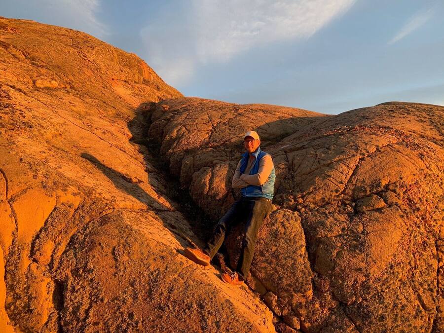 A person sitting on a rocky outcrop with a clear sky in the background.