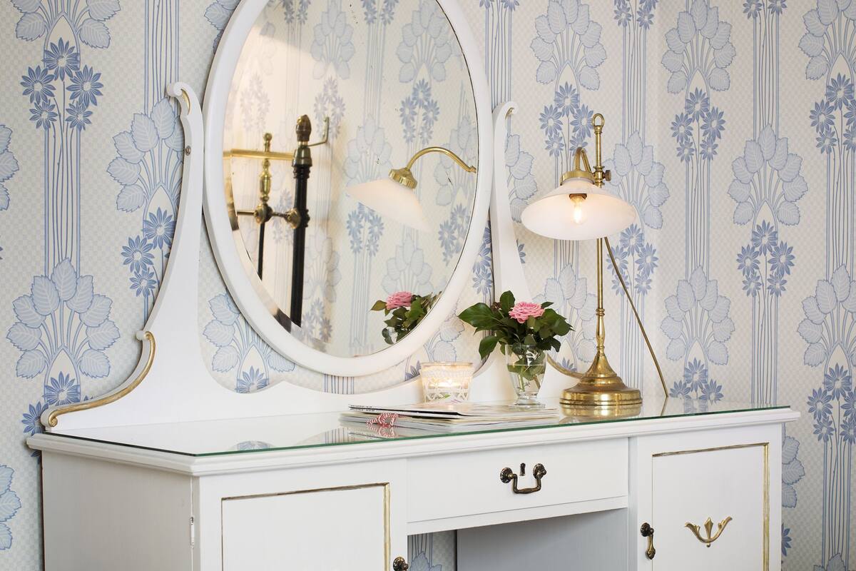 A bedroom with a bed, a dresser with a mirror, a lamp, and a vase with flowers.