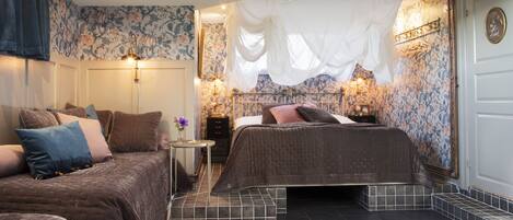 A bedroom with two beds, a nightstand, a small table with a vase, and a decorative wall with floral wallpaper.
