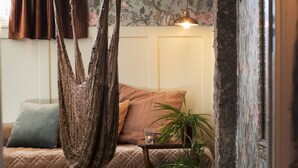 Een gezellige kamer met een hangstoel, een nachtkastje met een plant erop, en een lamp.
