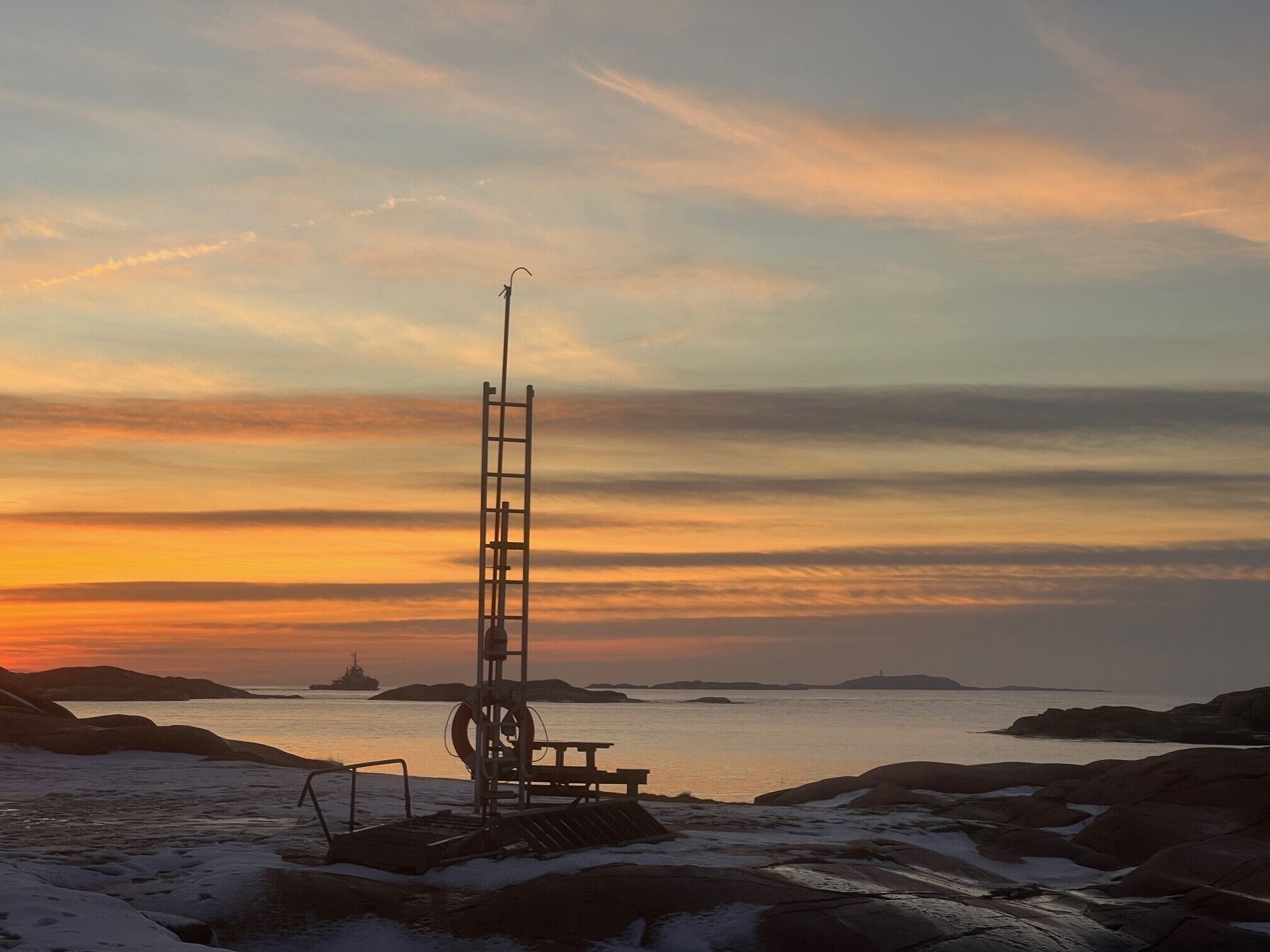 A lighthouse on a rocky shore with a sunset in the background.