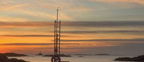 A lighthouse on a rocky shore with a sunset in the background.