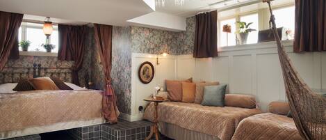 A bedroom with two beds, a hanging chair, a chandelier, and a window with curtains.