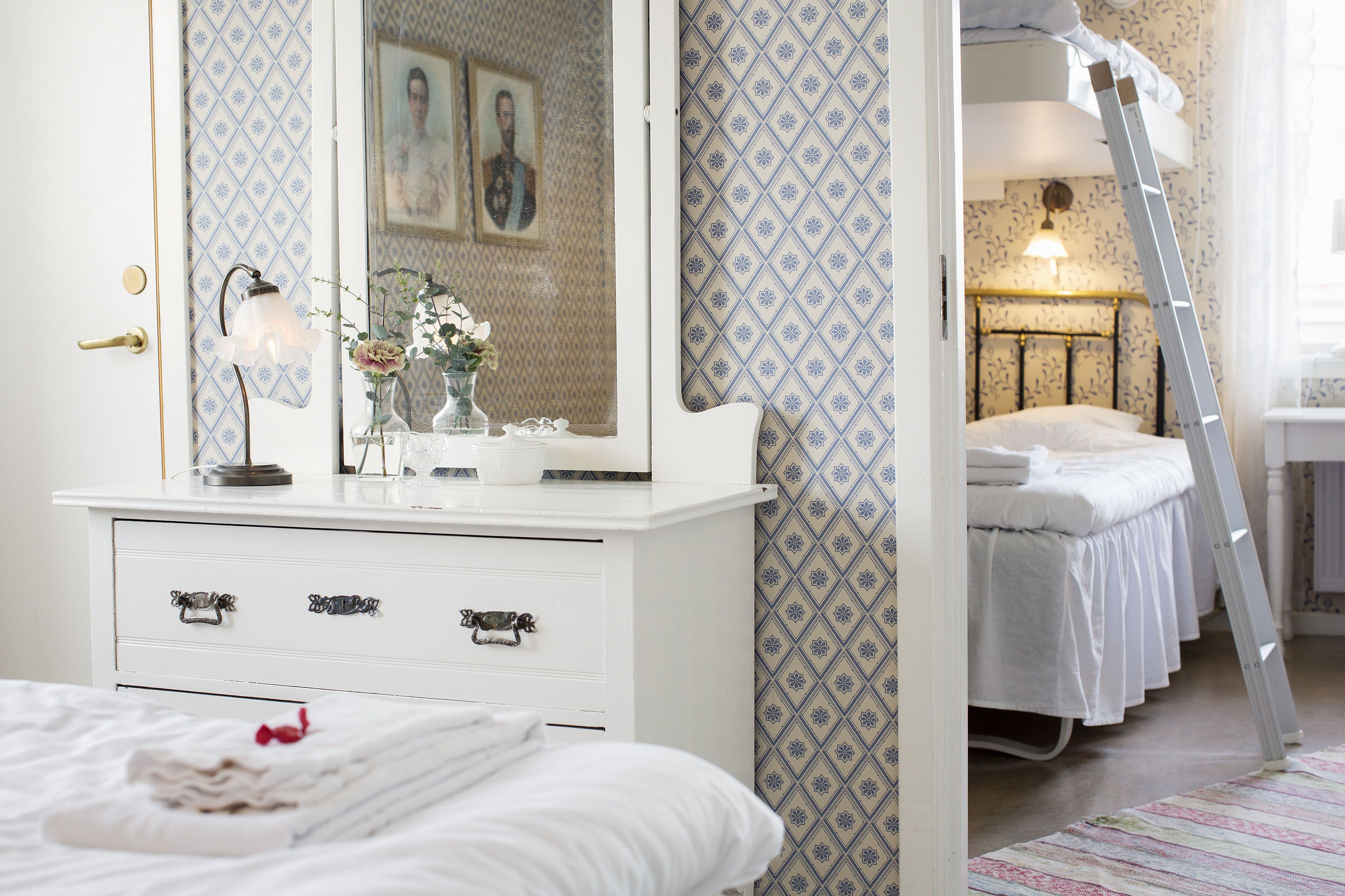 Un dormitorio con un aparador blanco, una cama con ropa de cama blanca y una escalera que lleva a una cama nido.