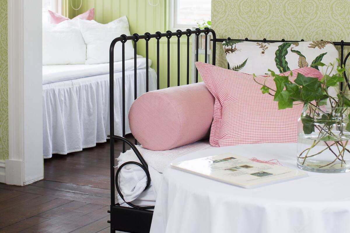 A room with a bed, a chair, and a table with a book and a vase.