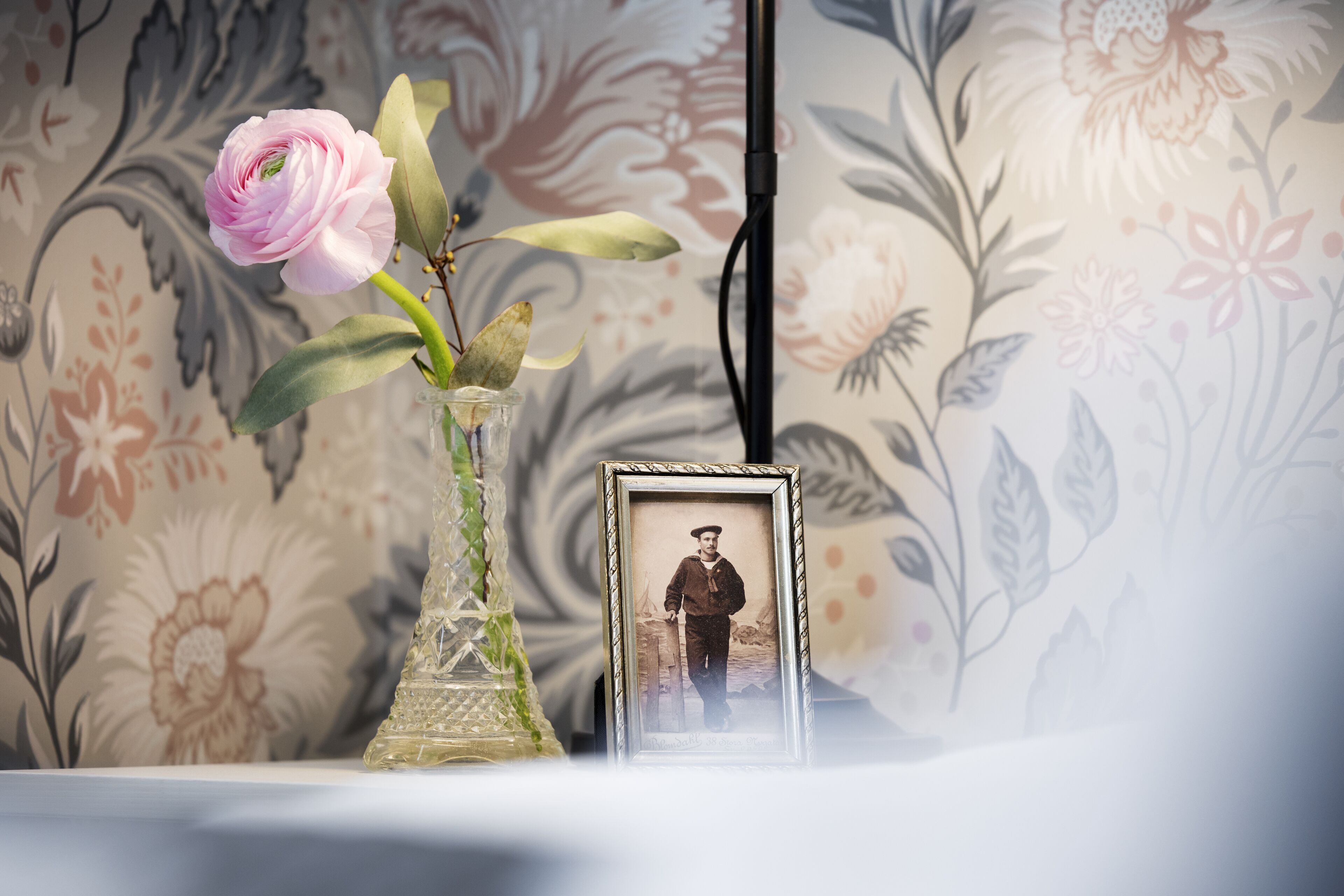 A vase with a pink flower and a framed photograph on a table.