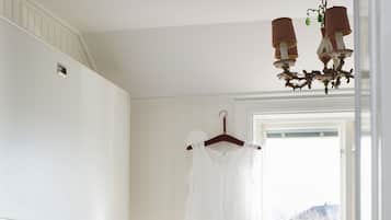 A bedroom with a bed, a dresser, a hanging garment, a sewing machine, and a window with a view.