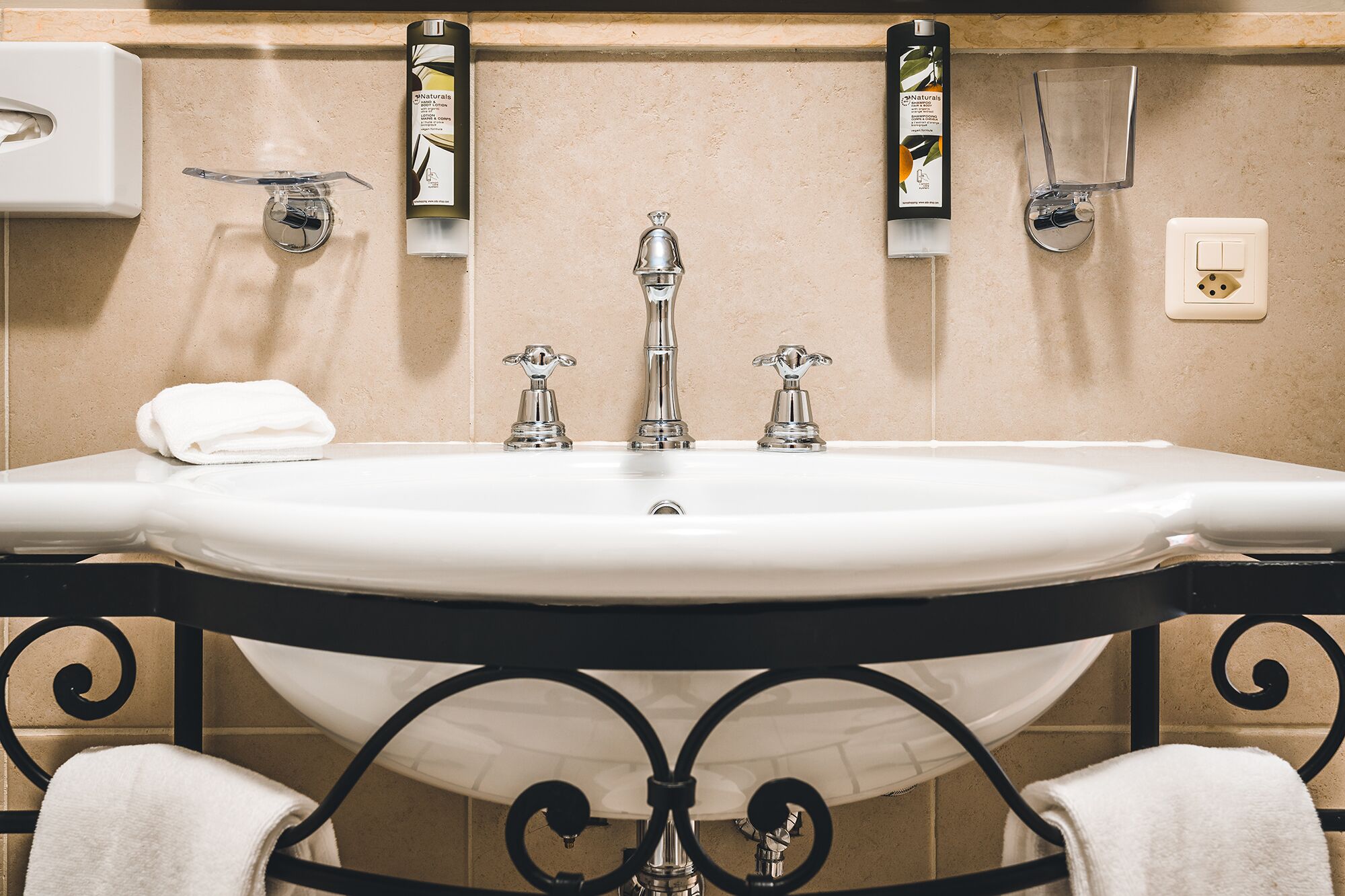 A bathroom with a white sink, two faucets, a towel rack, and toiletries on the wall.