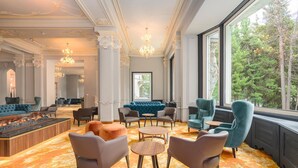 A luxurious lounge area with a fireplace, plush seating, and a large window offering a view of the forest. - Hotel Reine Victoria (St. Moritz)