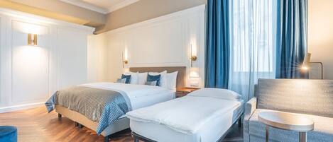 A hotel room with two beds, a sofa, a small table, and a blue chair.