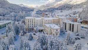 A hotel complex with multiple buildings, surrounded by snow-covered trees and mountains. - Hotel Reine Victoria (St. Moritz)